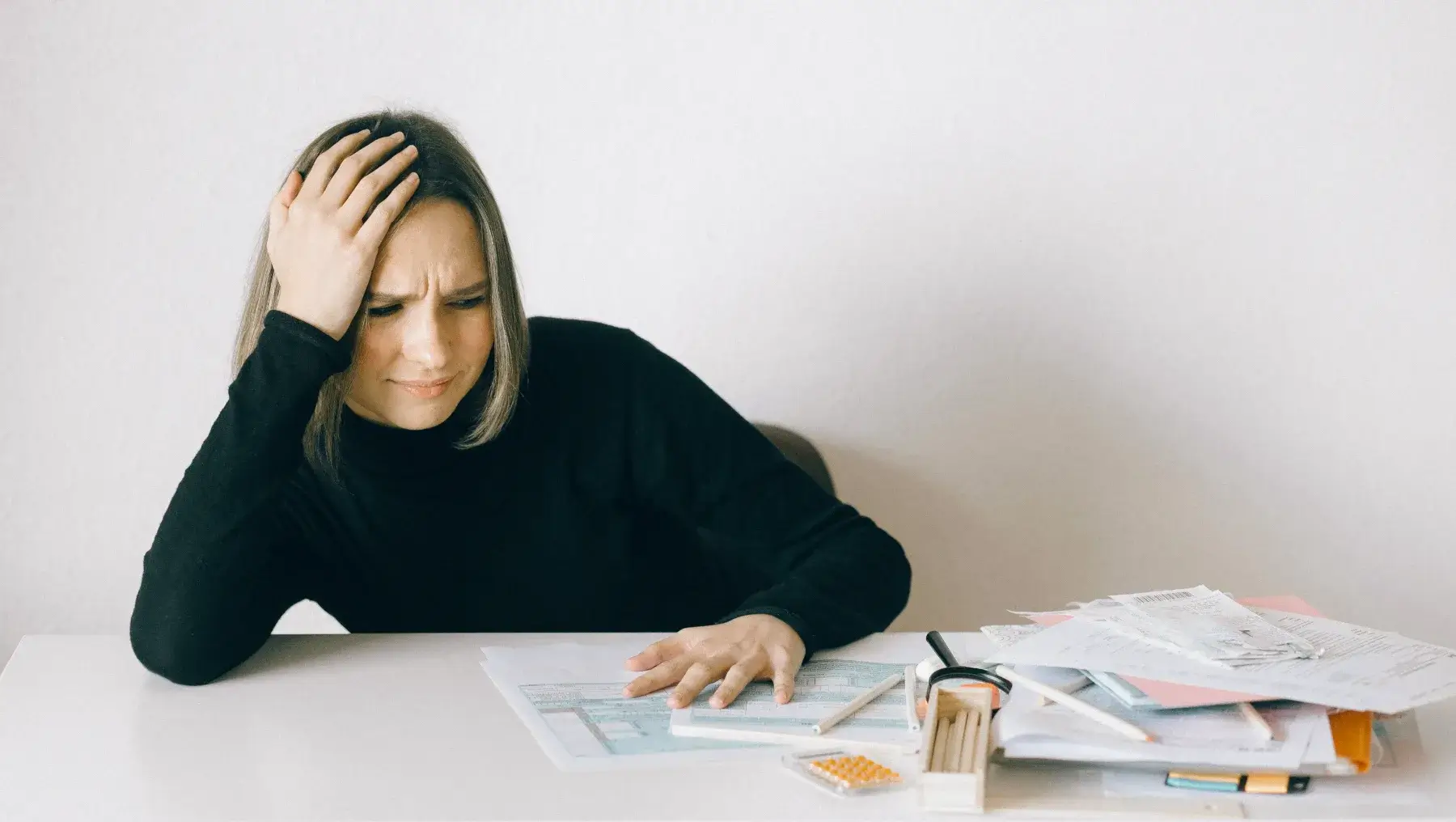 A woman sits at a desk with her hand on her head, looking frustrated while reviewing financial reports and documents—it's clear she might hate numbers.
